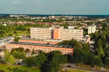 Kompleks szpitalny z pomarańczowo-białymi budynkami w otoczeniu zieleni, sfotografowany z lotu ptaka w słoneczny dzień.